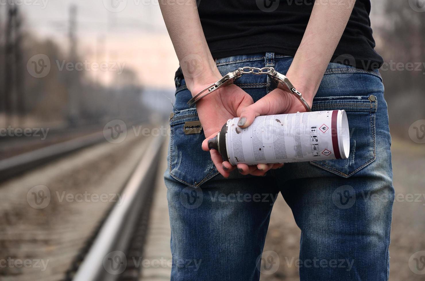 Girl in handcuffs with spraycan on the background of a railway track. The concept of vandalism prevention with the participation of the railway and trains. photo