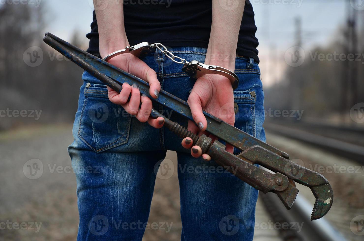 The girl in handcuffs with the pipe wrench on the railway track photo