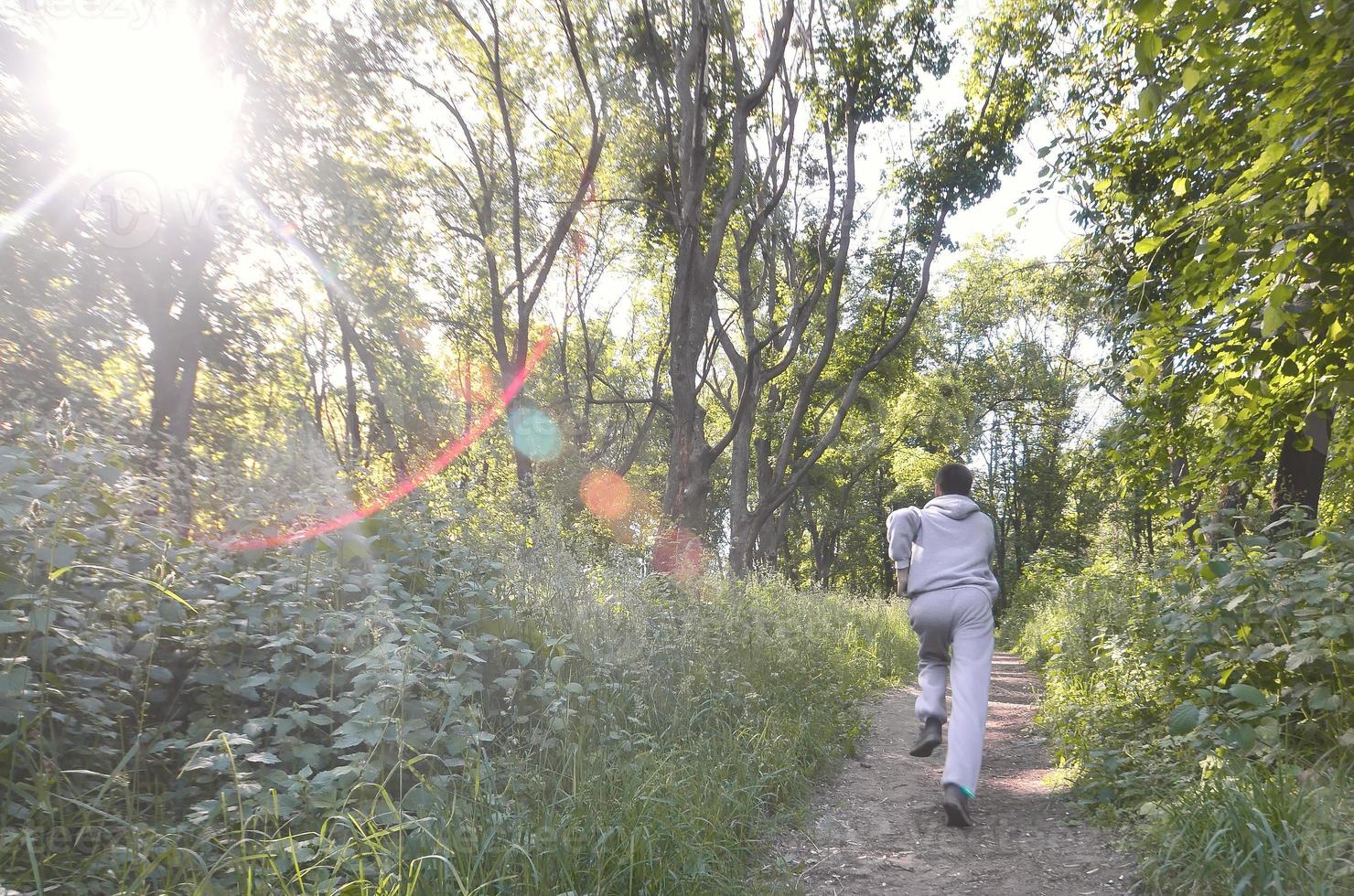 A young guy in a gray sports suit runs along the path among the photo