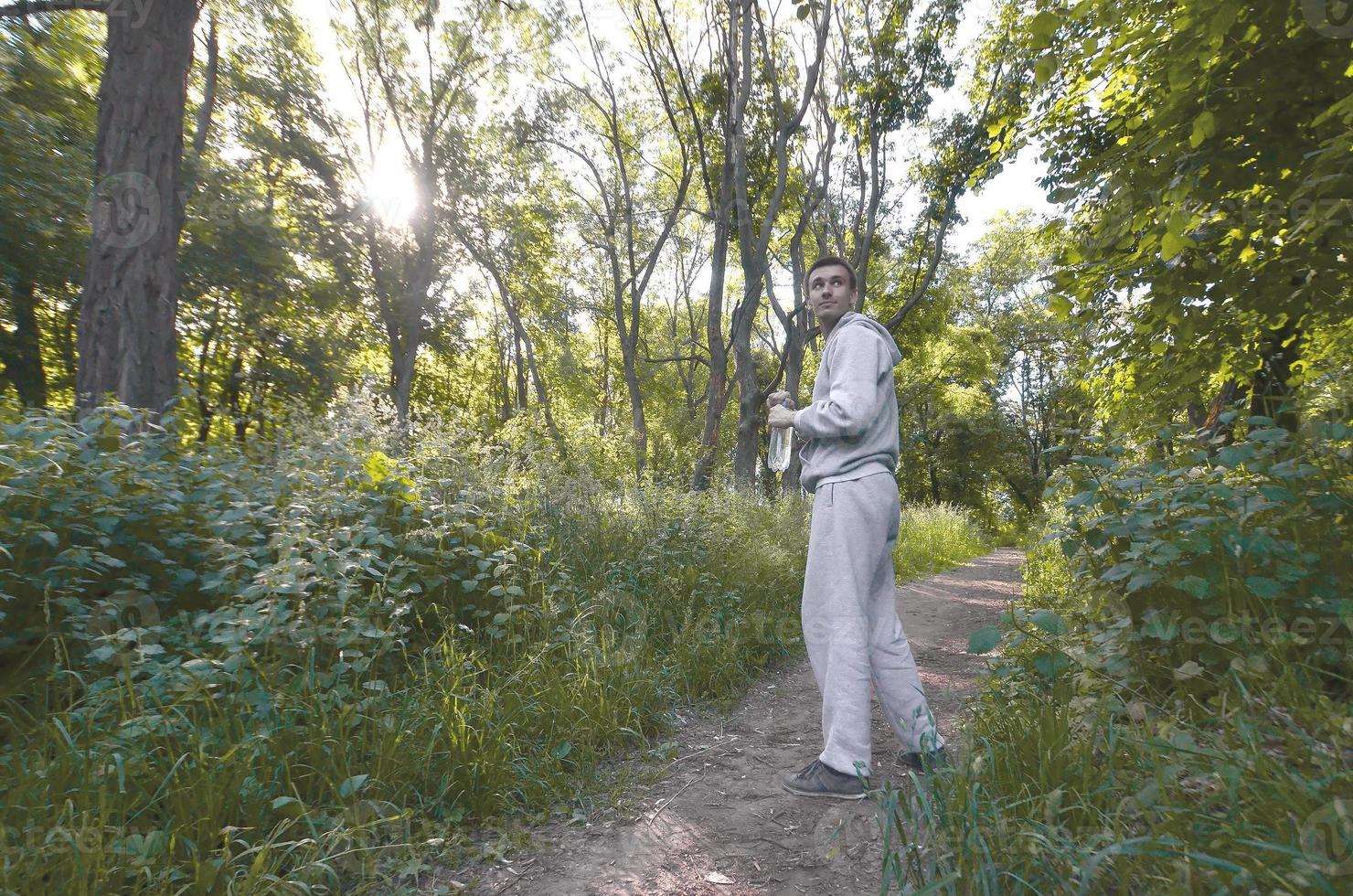 A young guy in a gray sports suit is standing with a bottle of w photo