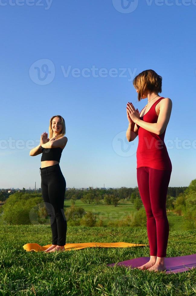 Two young fair-haired girls in sports suits practice yoga on a picturesque green hill in the open air in the evening. The concept of sport  exercising outdoors photo