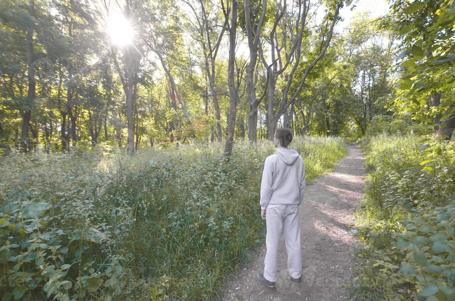 A young guy in a gray sports suit stands opposite the sun among photo