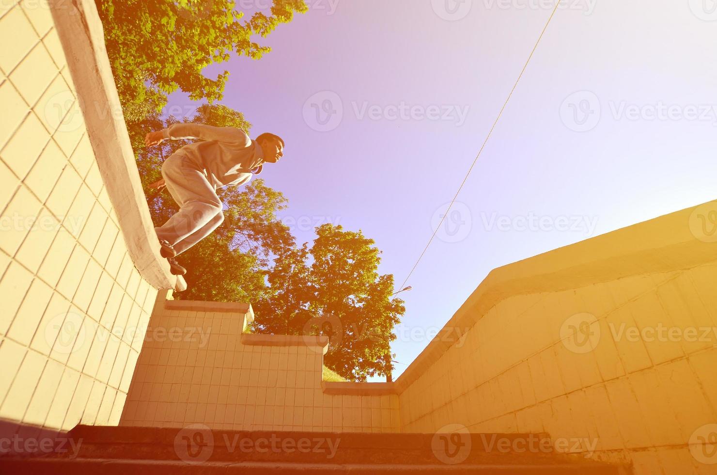 A young guy performs a jump through the space between the concrete parapets. The athlete practices parkour, training in street conditions. Bottom view photo