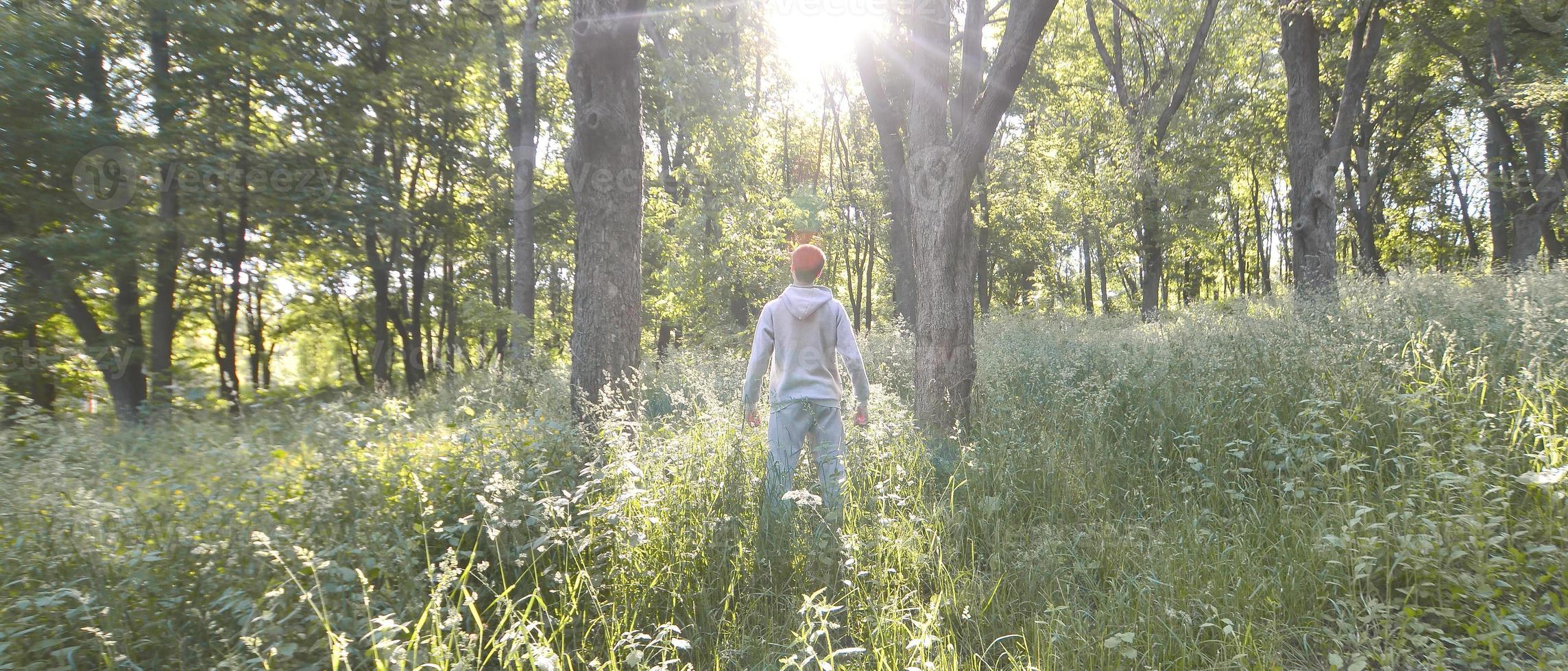 A young guy in a gray sports suit stands opposite the sun among photo