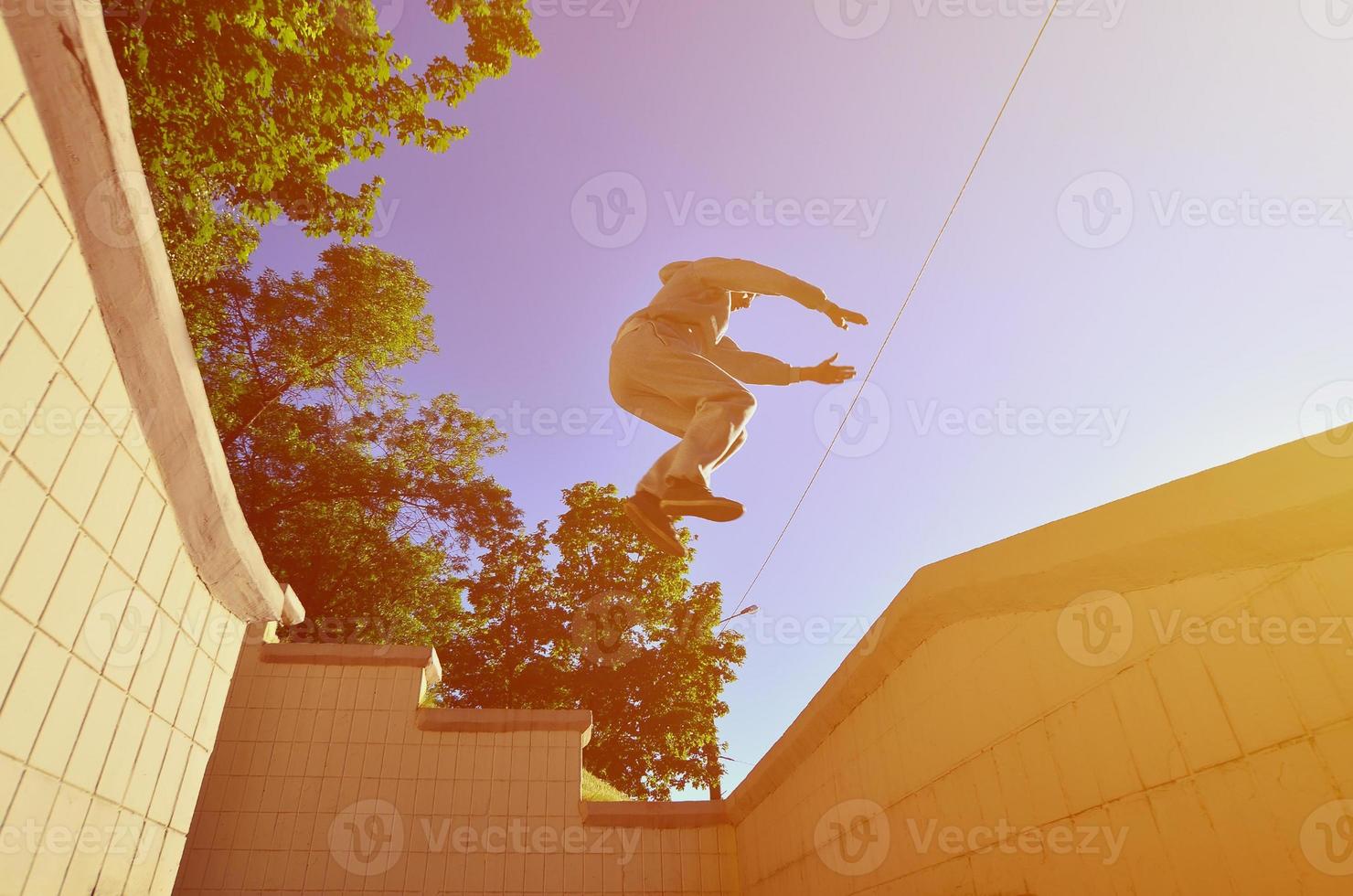 un chico joven realiza un salto a través del espacio entre los parapetos de hormigón. el atleta practica parkour, entrenando en condiciones de calle. vista inferior foto