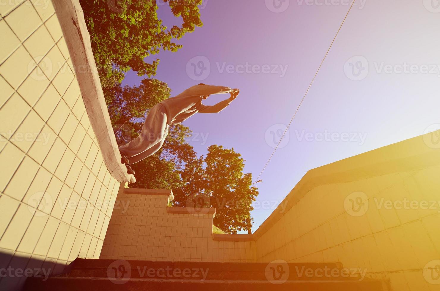 A young guy performs a jump through the space between the concrete parapets. The athlete practices parkour, training in street conditions. Bottom view photo