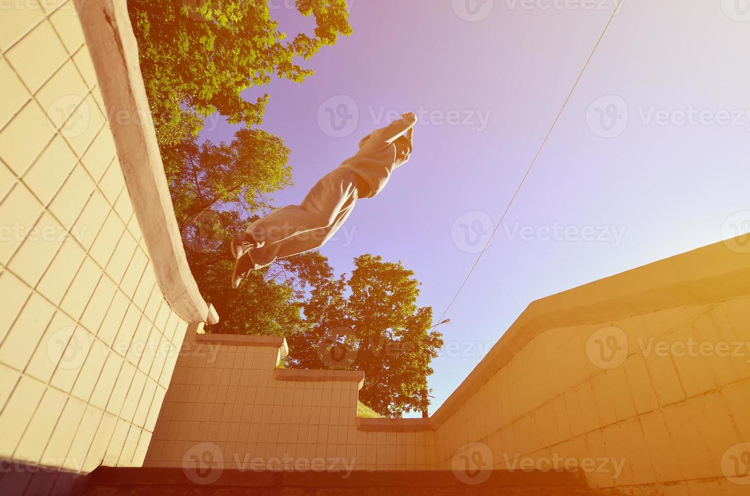 A young guy performs a jump through the space between the concrete parapets. The athlete practices parkour, training in street conditions. Bottom view photo