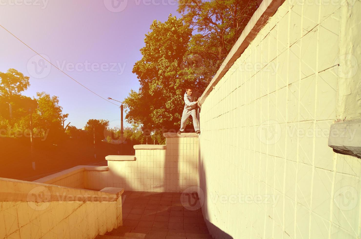 A young guy overcomes obstacles, climbing on concrete walls. The athlete practices parkour, training in street conditions. The concept of sports subcultures among youth photo