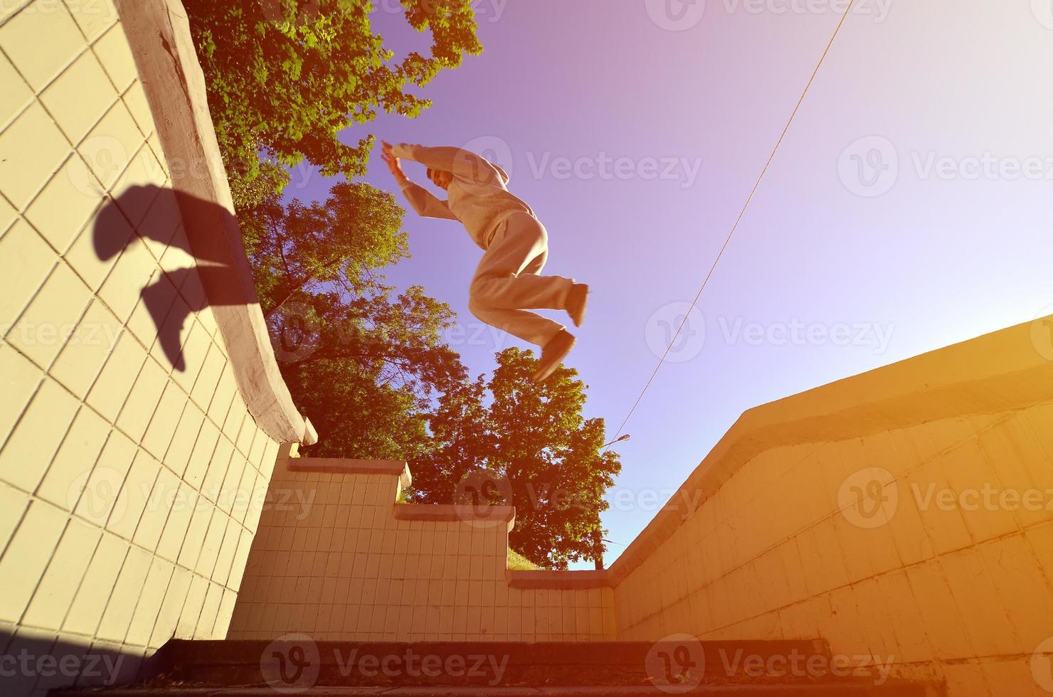 A young guy performs a jump through the space between the concrete parapets. The athlete practices parkour, training in street conditions. Bottom view photo