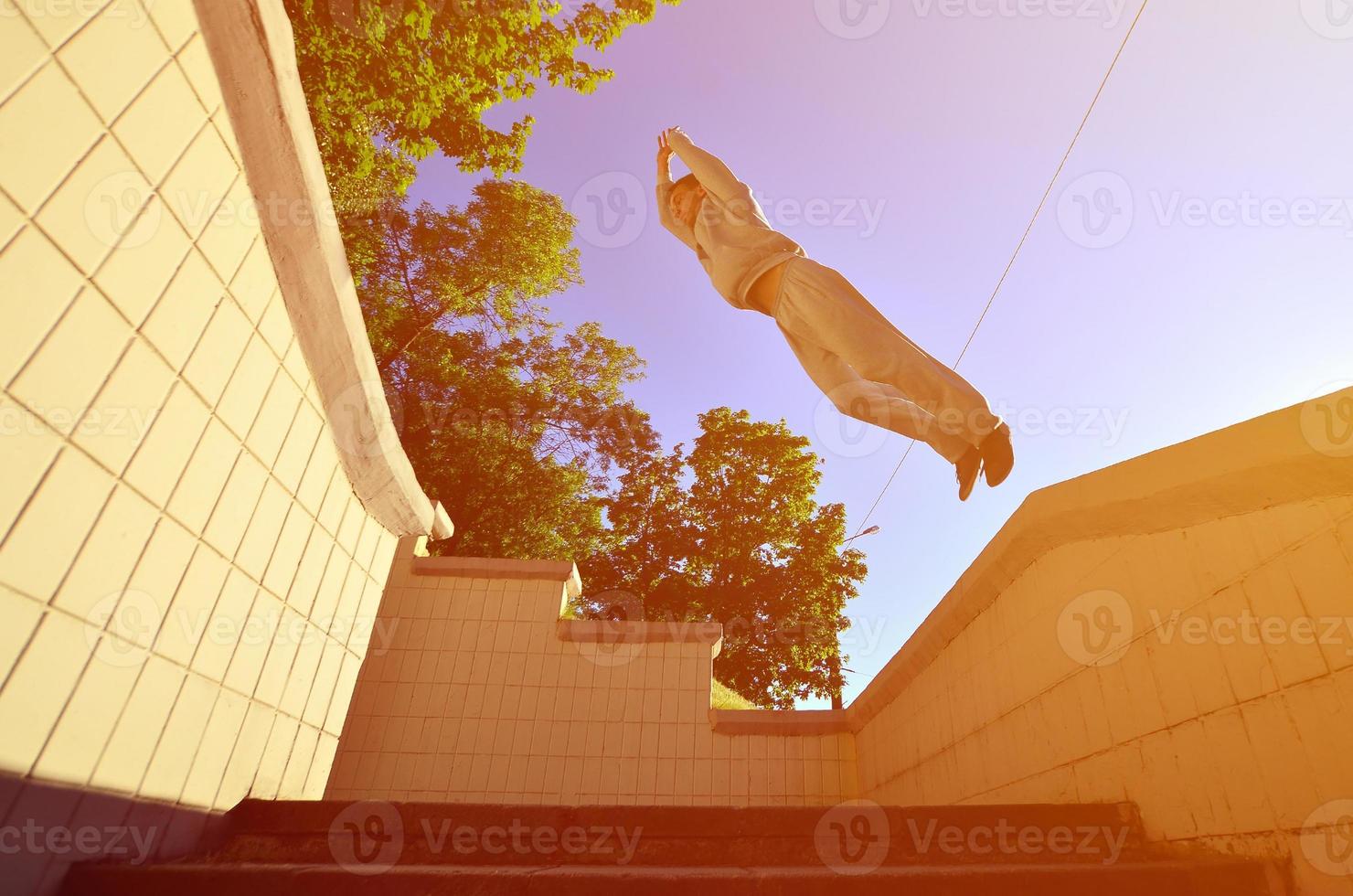 A young guy performs a jump through the space between the concrete parapets. The athlete practices parkour, training in street conditions. Bottom view photo