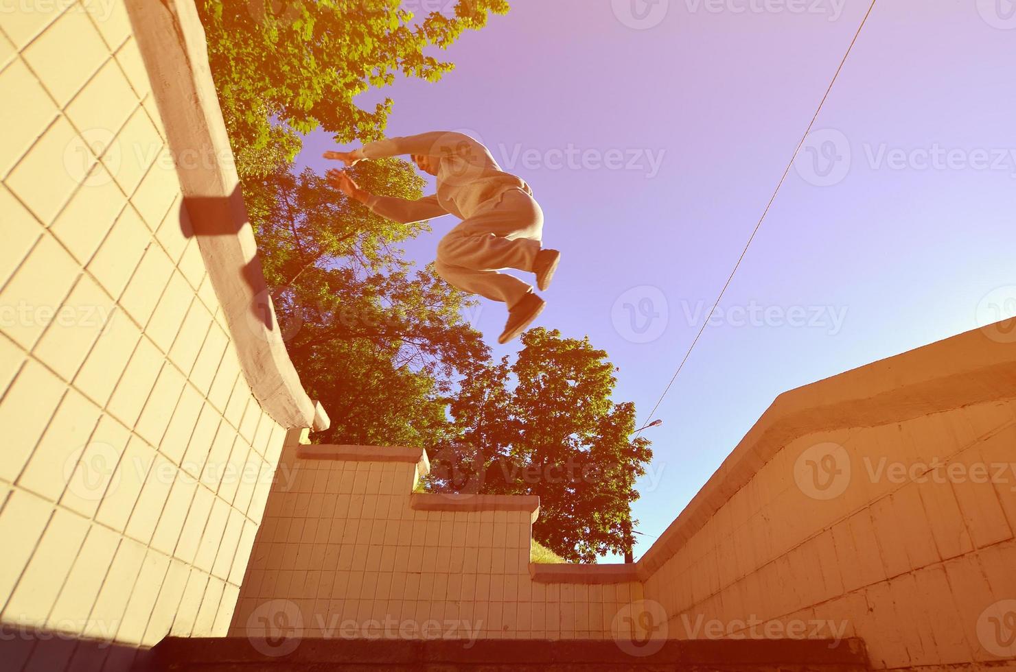 A young guy performs a jump through the space between the concrete parapets. The athlete practices parkour, training in street conditions. Bottom view photo