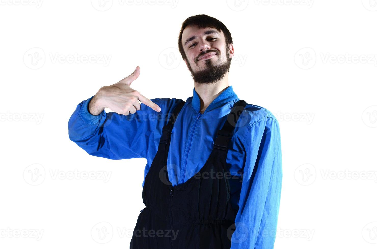 A young bearded guy in working uniform points to himself with his finger. A proud worker takes praise and encouragement to his person. Isolated on white photo