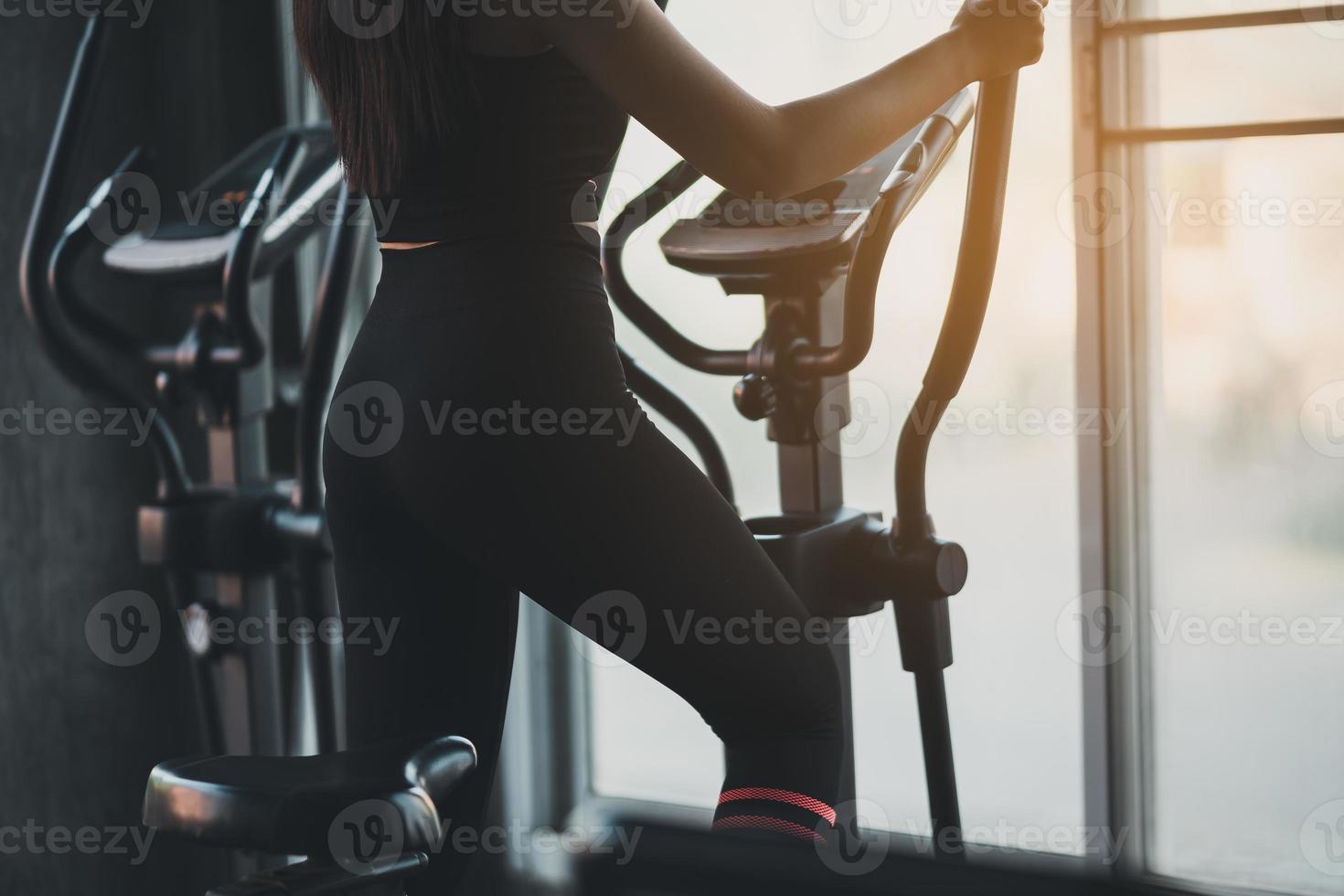 Crop picture, back view, sportswoman exercising on elliptical machine in the gym, determination to cardio lose weight, makes her healthy. exercise elliptical machine woman fitness sport concept. photo
