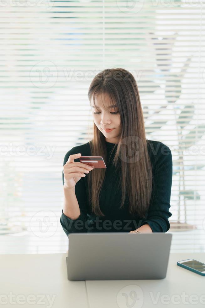 Asian woman holding credit card and using laptop computer. Businesswoman working at home. Online shopping, e-commerce, internet banking, spending money, working from home concept. photo