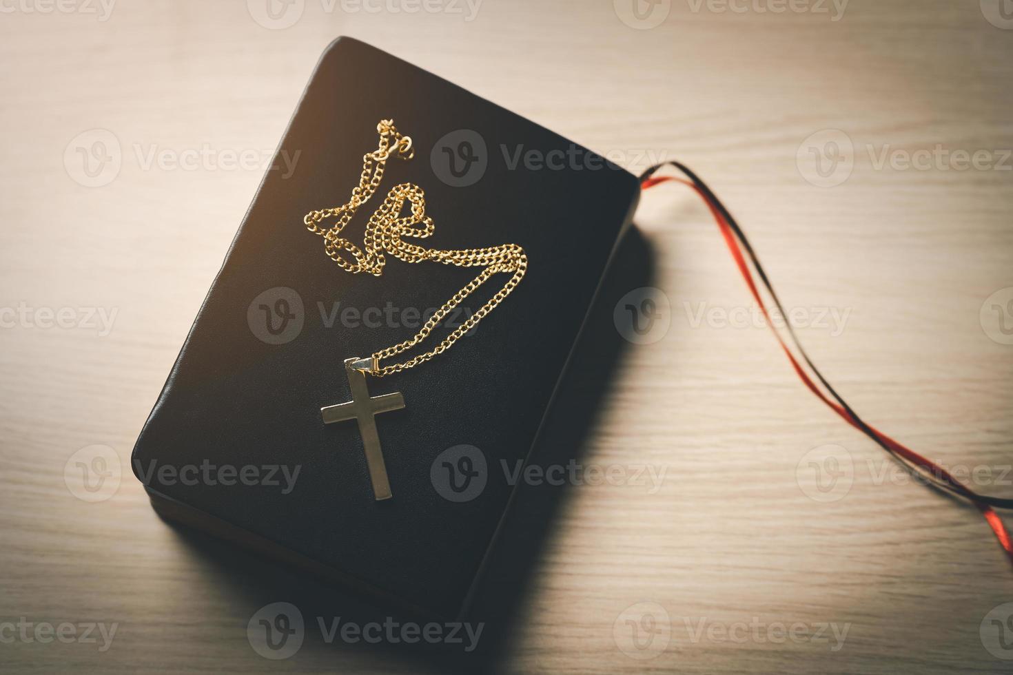 Close up top view Christian gold stainless steel crucifix necklace crosses placed on bible black leather cover place on a wooden table. Spirituality and religion. Christian prayer religion concept. photo