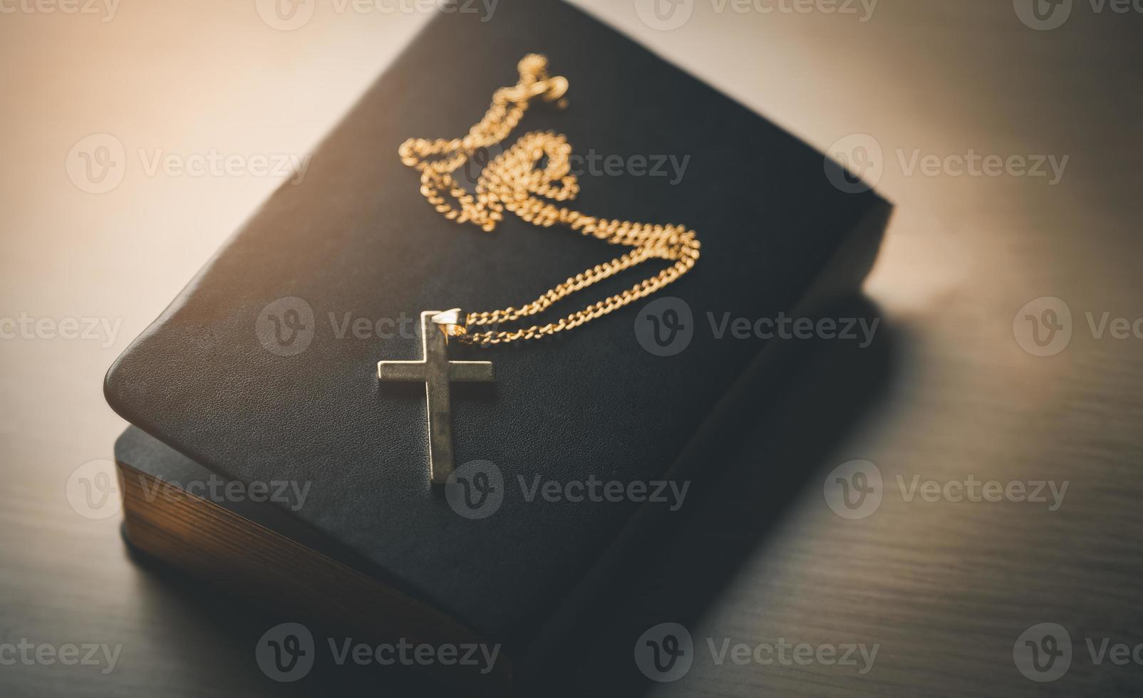 Close up top view Christian gold stainless steel crucifix necklace crosses placed on bible black leather cover place on a wooden table. Spirituality and religion. Christian prayer religion concept. photo