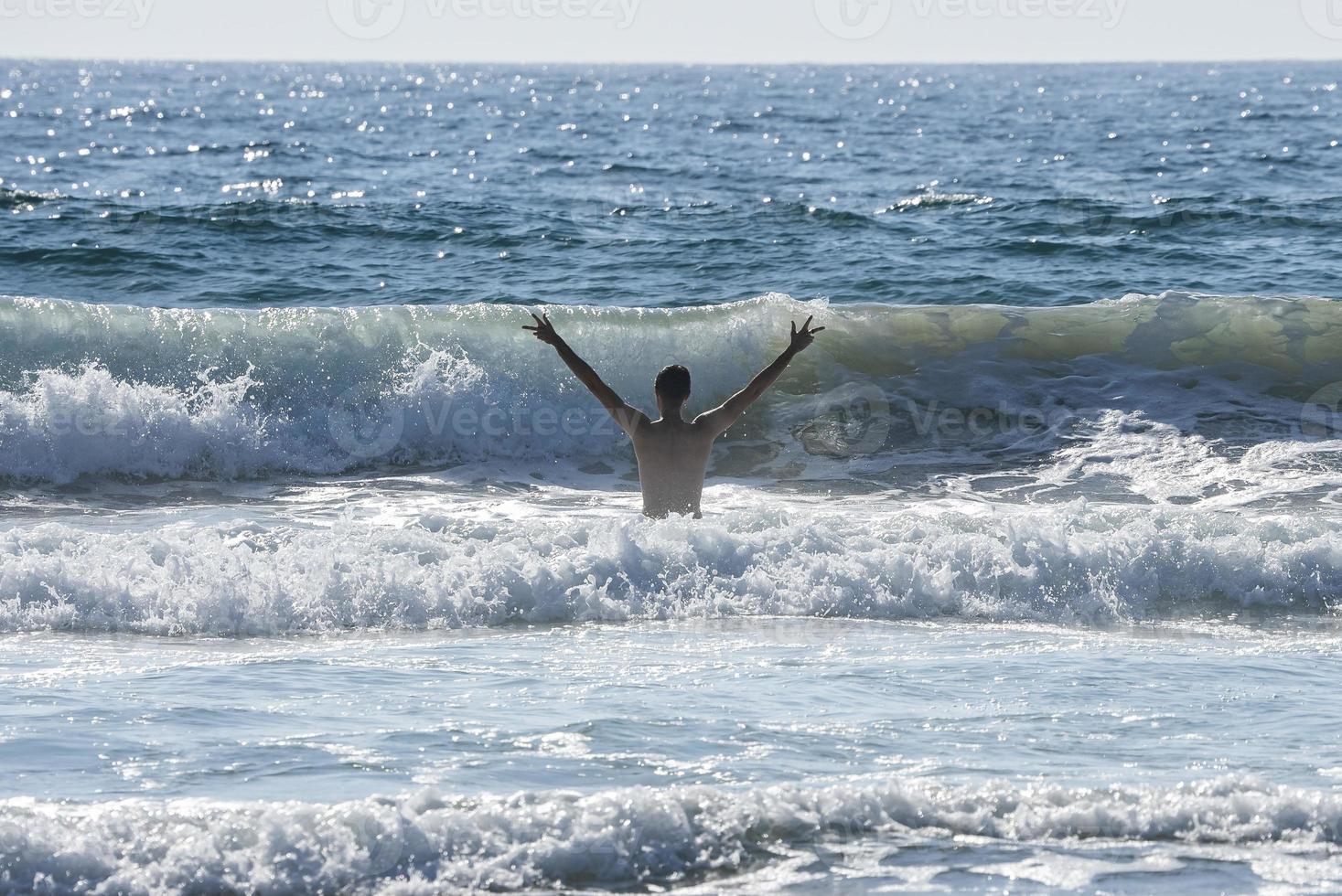 Carefree shirtless man with arms raised standing amidst sea photo