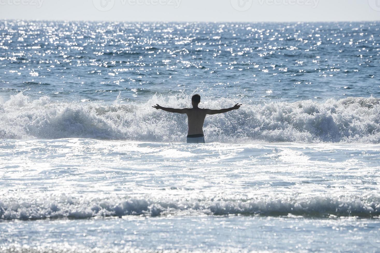 Carefree shirtless man with arms outstretched standing amidst sea photo