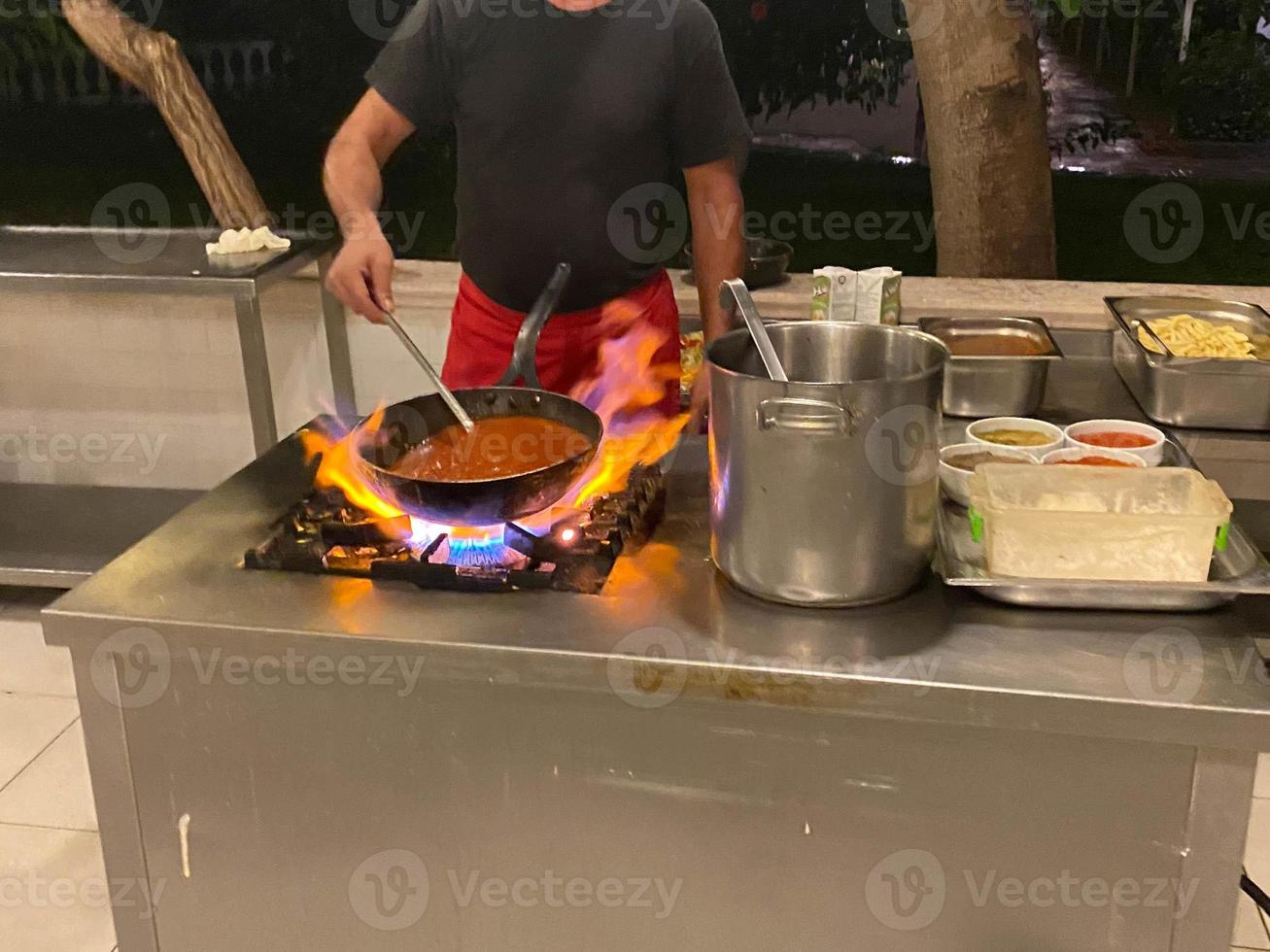 Chef, cook cooking in a frying pan on fire food in a restaurant in an open kitchen in an all-inclusive hotel in a touristic warm tropical country paradise resort on vacation photo