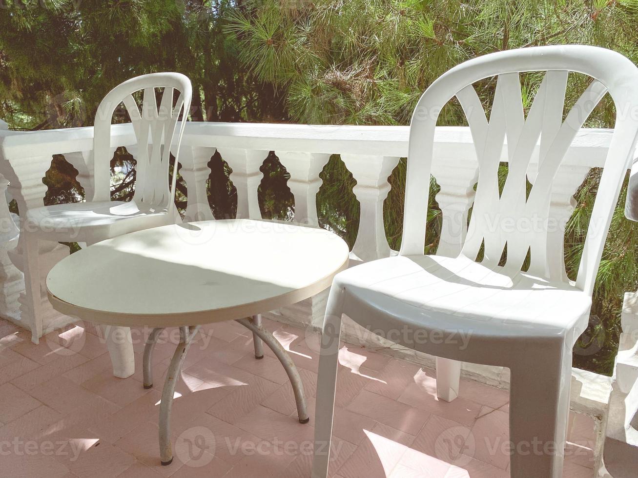 plastic furniture on the balcony. small round table with white chairs. places for rest of tourists and people. balcony at a height against the backdrop of a spruce forest photo