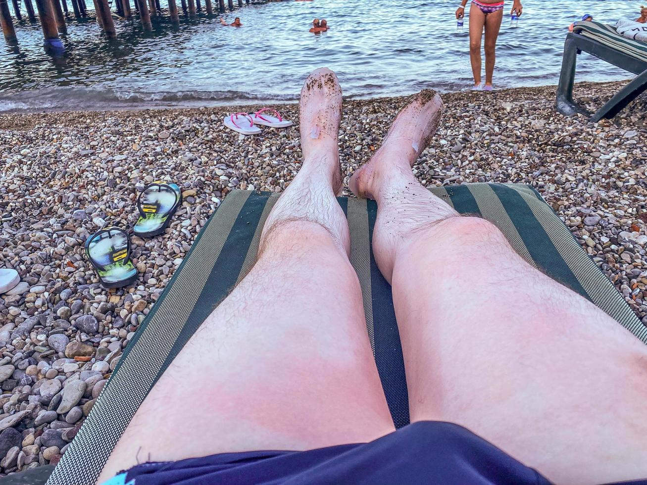 hot, tropical country with sea and mountains. pebbles on the beach, small stones near the water. there is a sunbed on the ground, on which lies a man with dirty feet photo