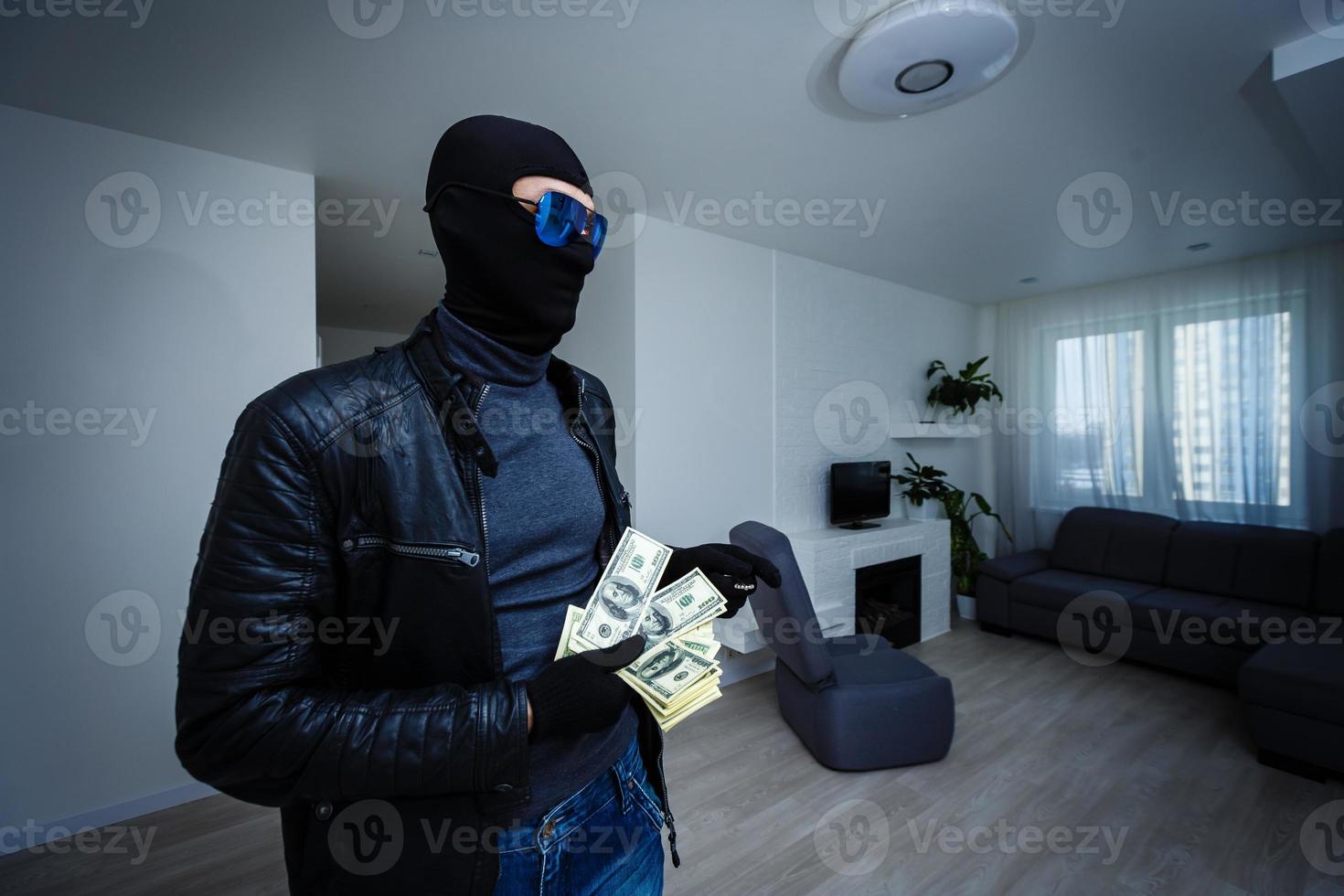 Robber man dressed in black hoodie stands with disguised face and holds a lot of money in his hands, stole a large amount, a thief man stole a TV photo