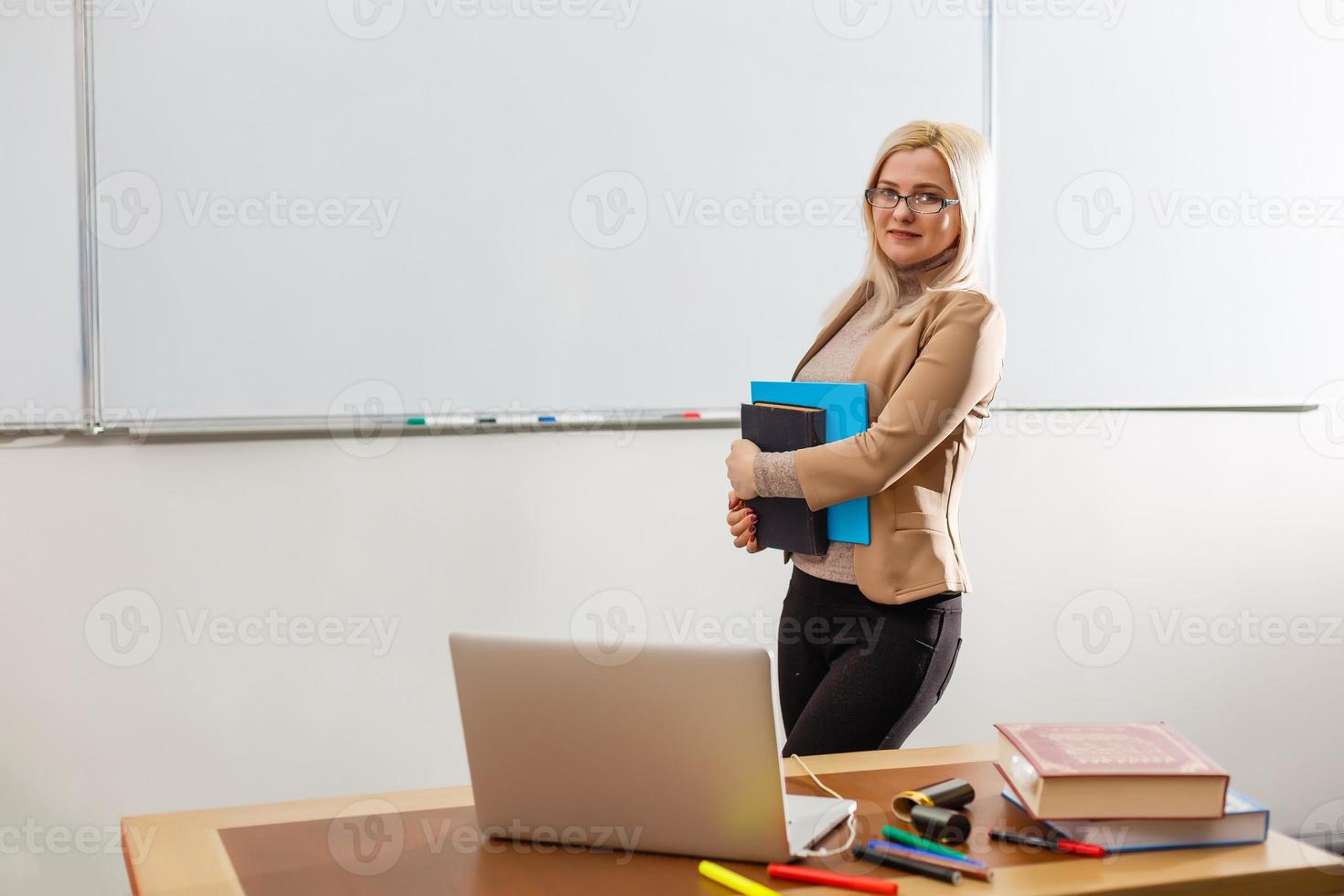 linda maestra sonriendo a la cámara en la parte de atrás del salón de clases en la escuela primaria foto