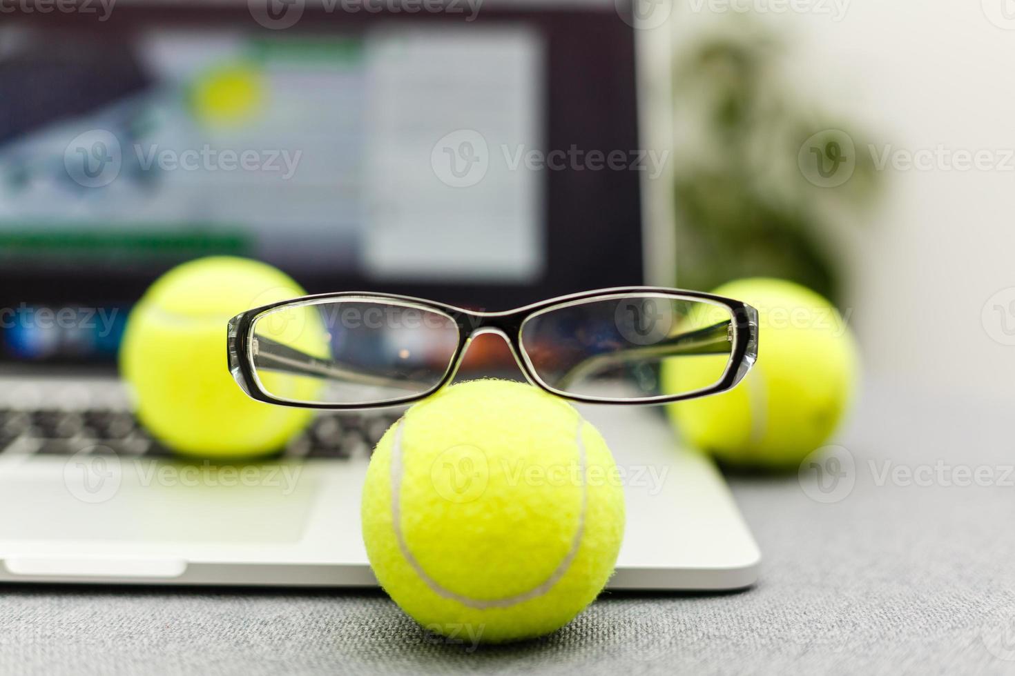 Top view of laptop, Sports Equipment, Tennis ball, glasses on the Sports administration white table.Business concept. photo