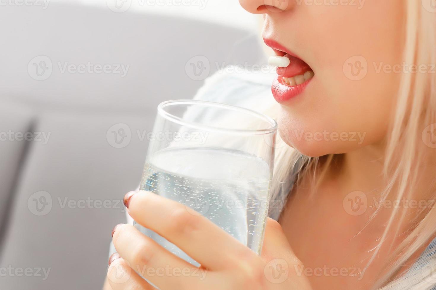 Happy young woman sitting on sofa and taking pill photo