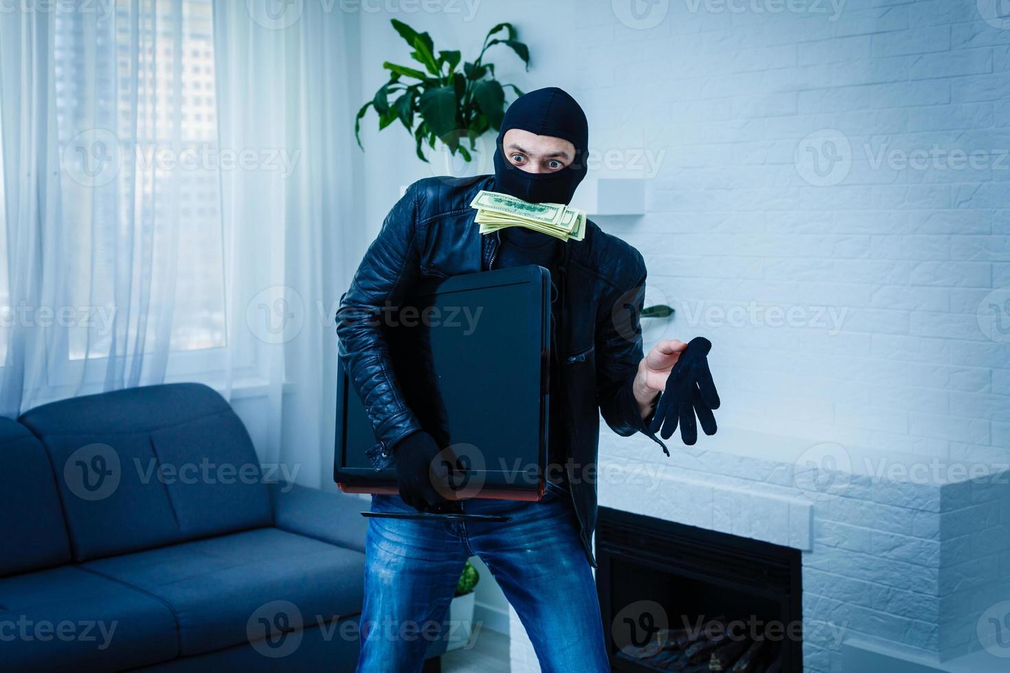 Robber man dressed in black hoodie stands with disguised face and holds a lot of money in his hands, stole a large amount, a thief man stole a TV photo