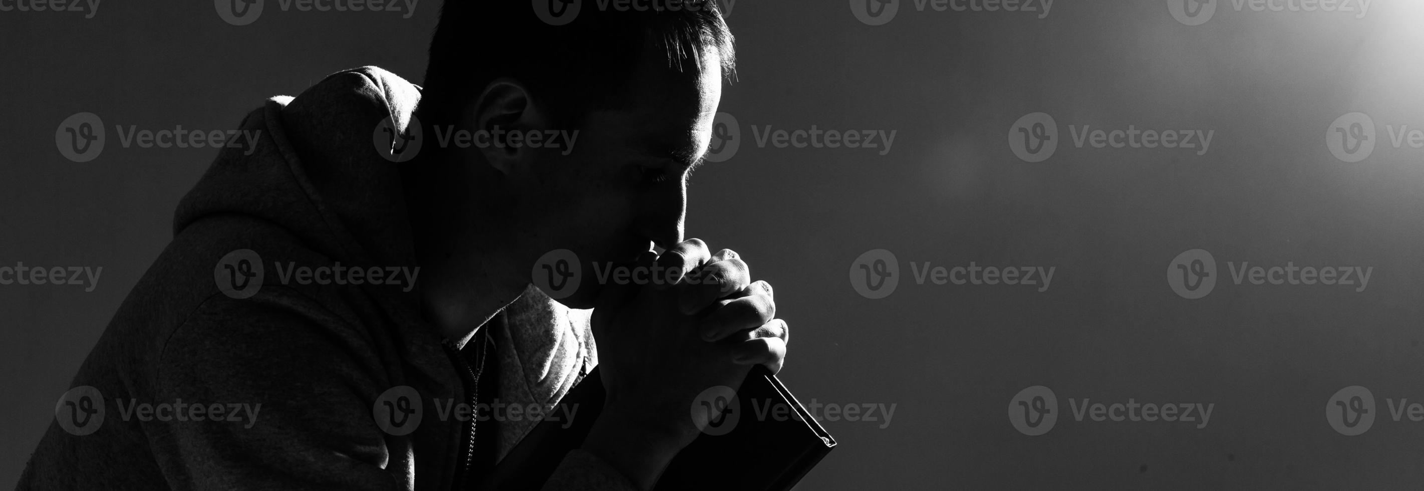 Religious young man praying to God on dark background, black and white effect photo