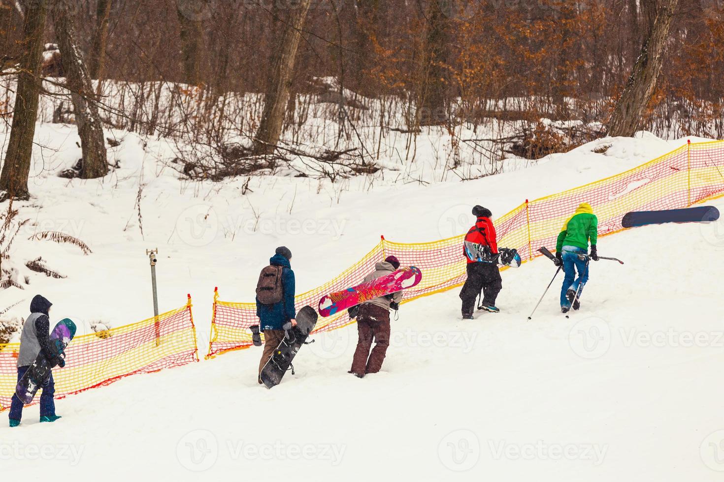 Joyful snowboarders, with snowboards in their hands, go up the mountain slope, amidst huge snow-covered fir trees at sunny day and enjoying life. Epic freeride in a winter wilderness. photo