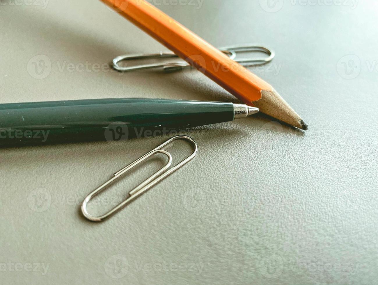 stationery on the table in the office. a blue metal pen for writing, a simple wooden pencil with lead. next to two metal paper clips for documents photo