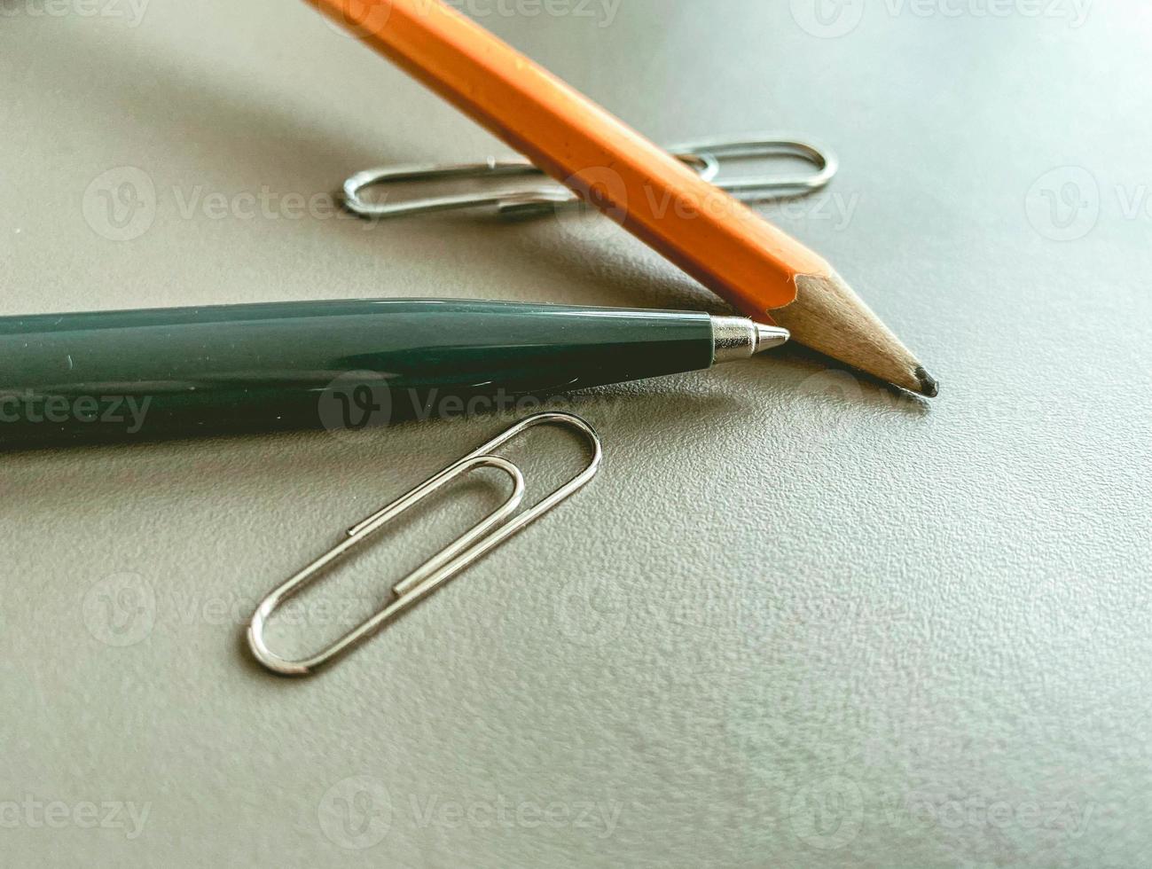 papelería en la mesa de la oficina. una pluma de metal azul para escribir, un simple lápiz de madera con mina. junto a dos clips metálicos para documentos foto