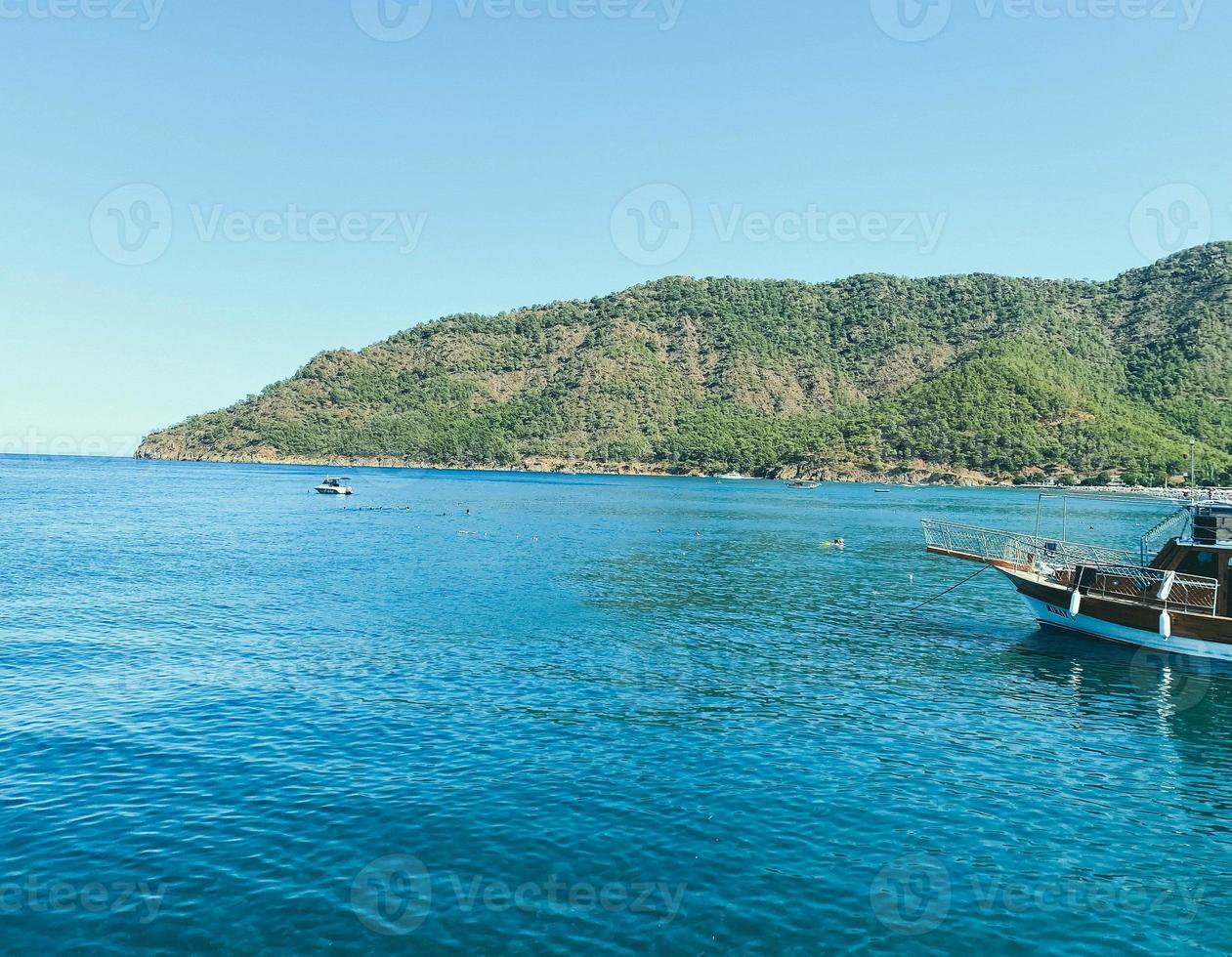 sea coast. blue waves of sea water with white foam. the sea at the foot of the mountain with plants and trees at the top. holidays in a hot country photo