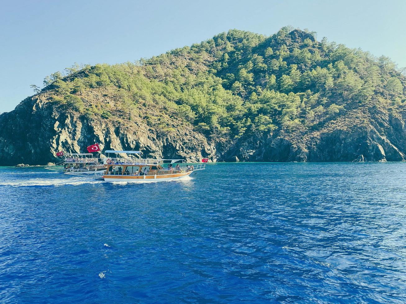 costa del mar vista desde el yate al agua y las montañas. viajar a un país cálido y exótico. montaña con vegetación. un barco con turistas flota en el mar foto