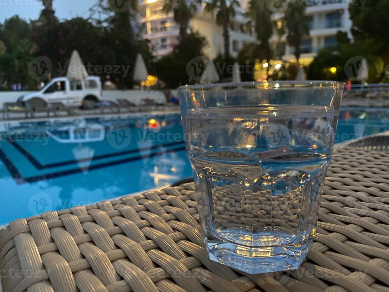 vaso con cóctel de naranja frente a una piscina con agua clara foto