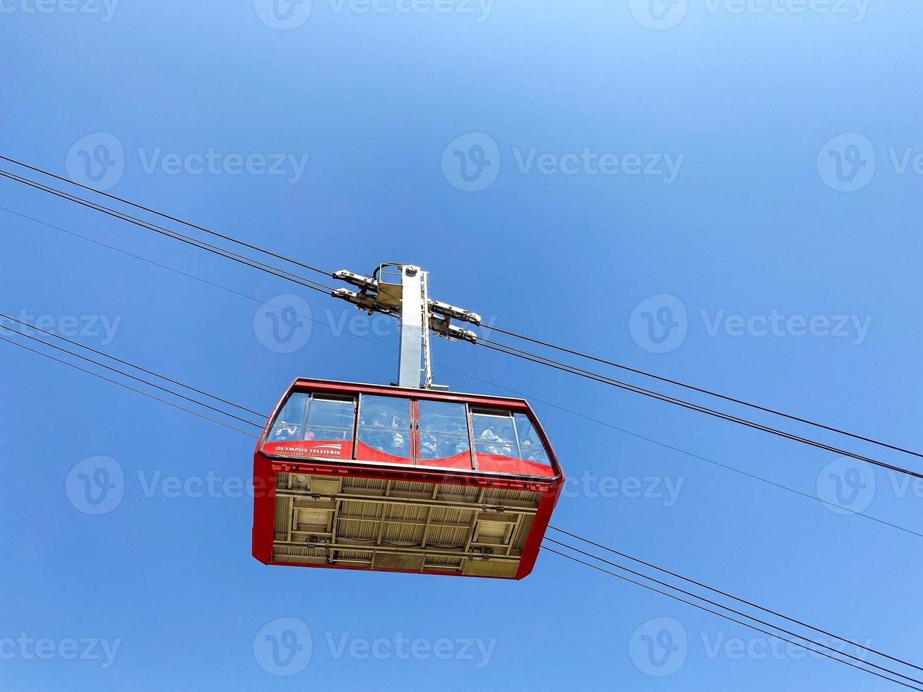 cable car on the mountain. cabin with tourists moves on black, thick cables at a great height. red cabin with large windows for viewing, there are a lot of people inside photo