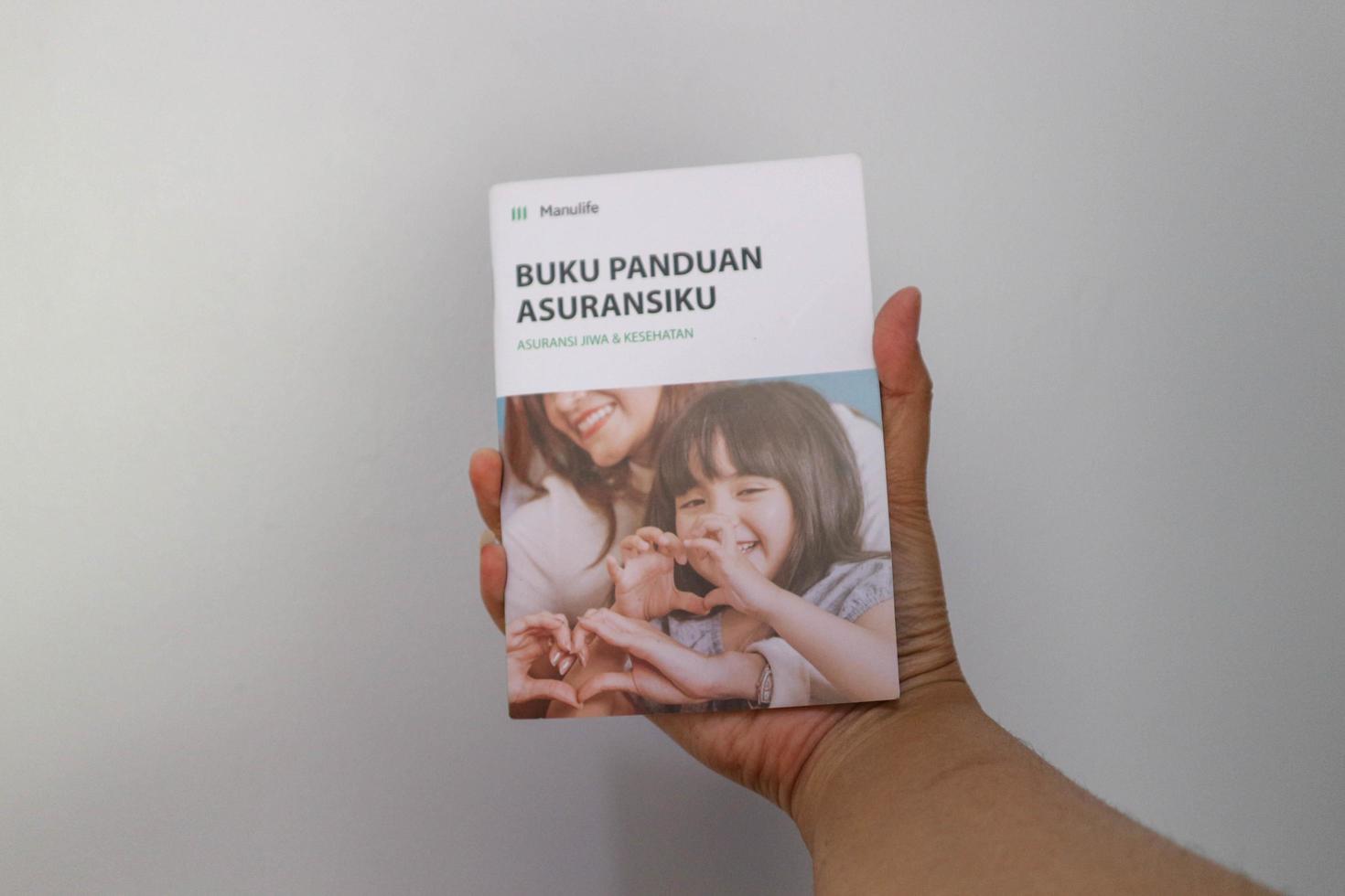 West Java, Indonesia on July 2022. A hand holding Manulife's Insurance Handbook for life and health insurance photo