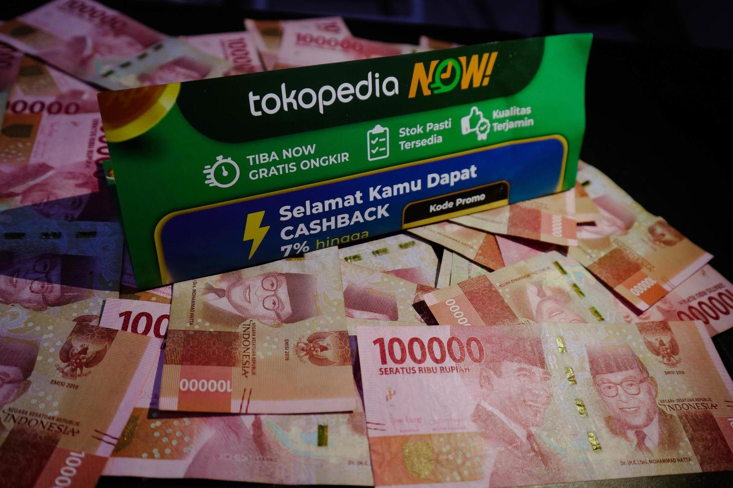 Jakarta, Indonesia in December 2022. A Tokopedia Now flyer above several hundred thousand rupiah notes scattered around. photo