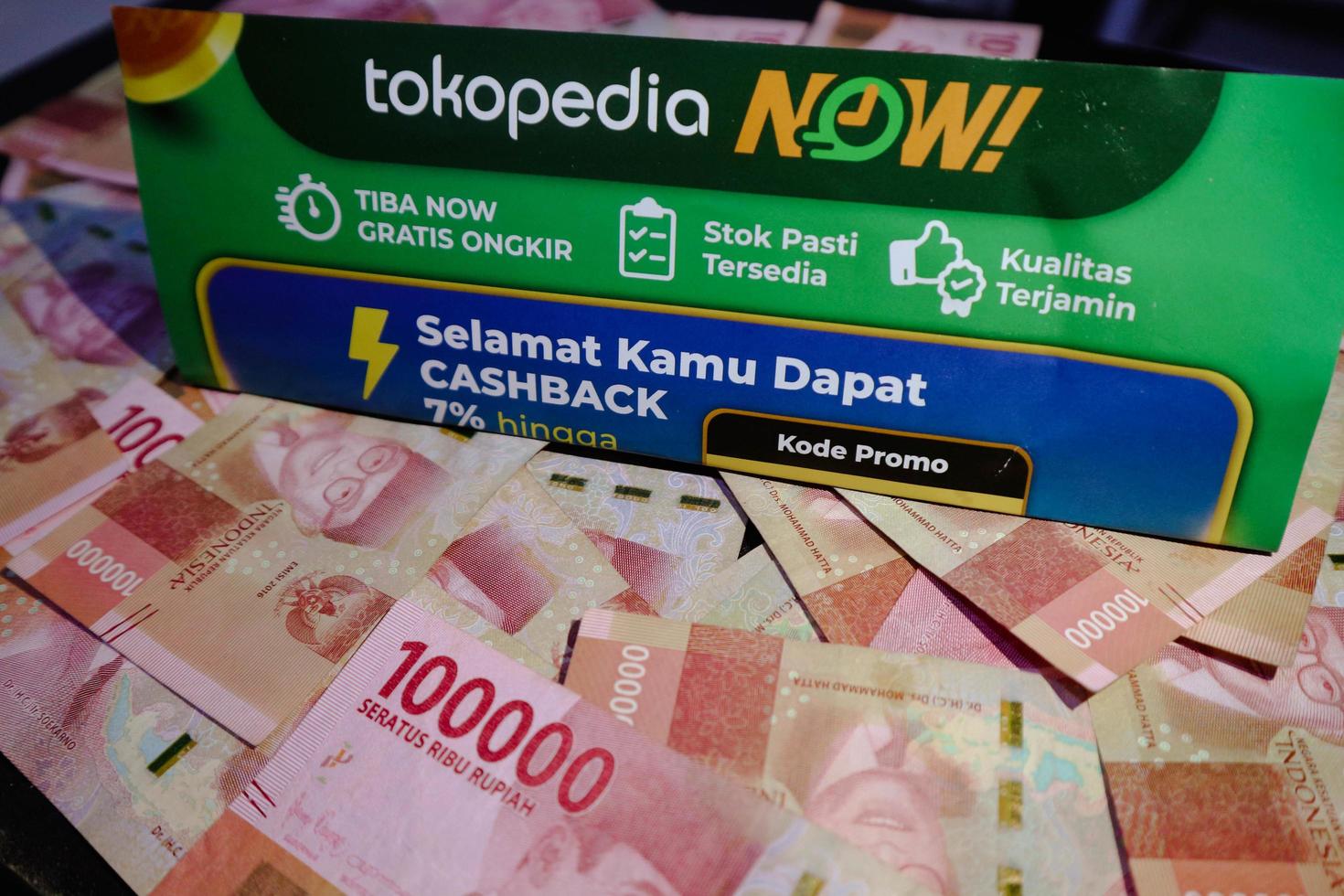 Jakarta, Indonesia in December 2022. A Tokopedia Now flyer above several hundred thousand rupiah notes scattered around. photo
