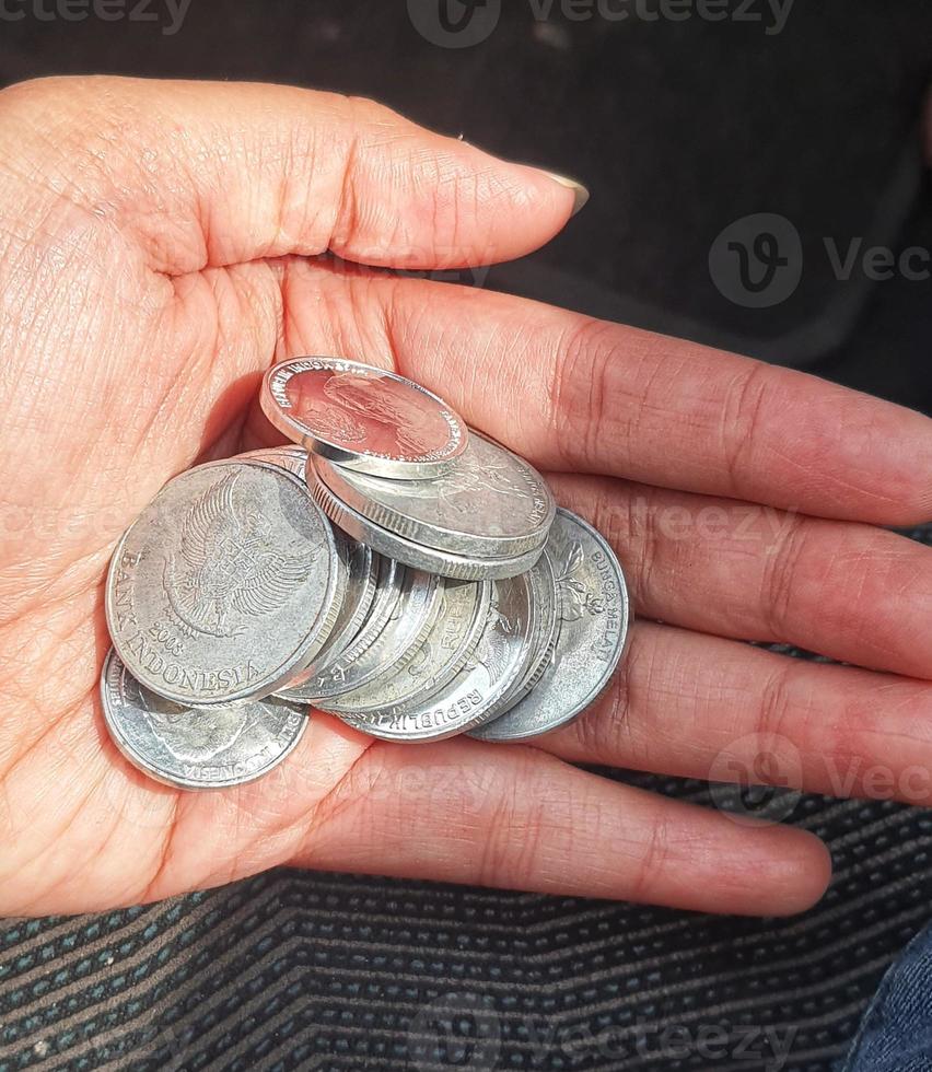 A hand is holding several rupiah coins. These coins are usually used to give to packs of people who help cross the vehicle or direct them to turn around. photo