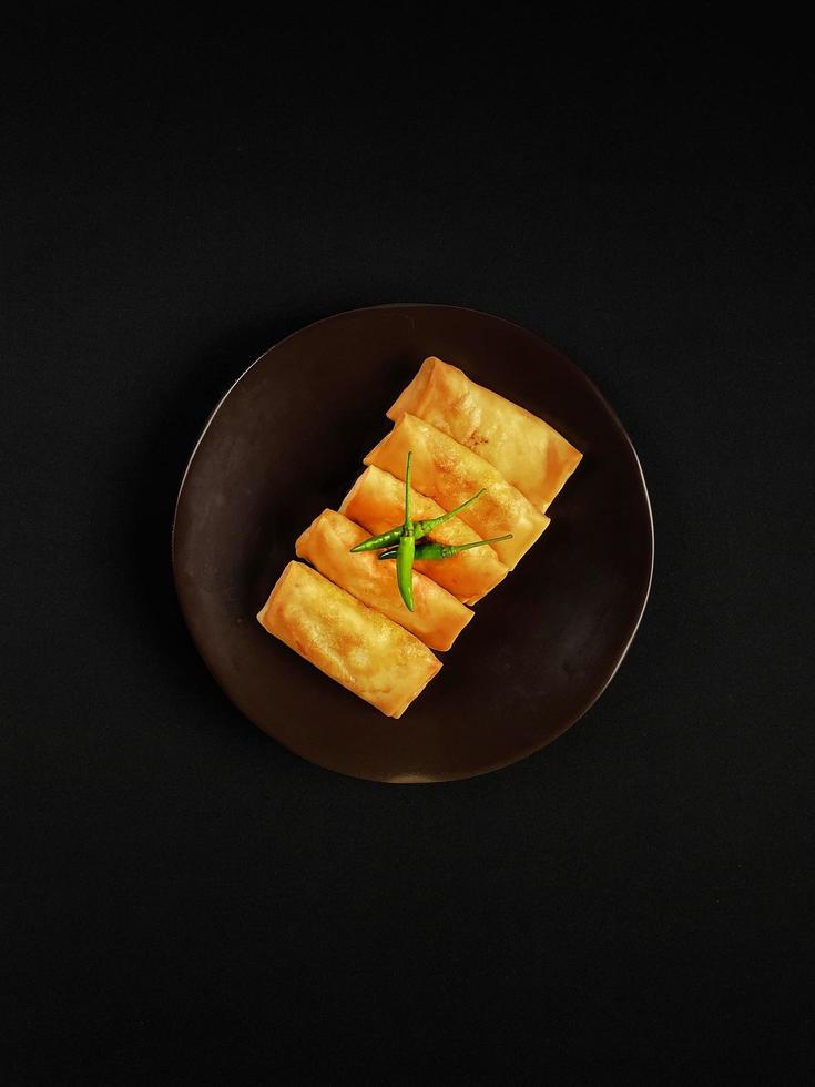 Mini martabak garnished with green chili peppers on the brown ceramic plate with black background photo