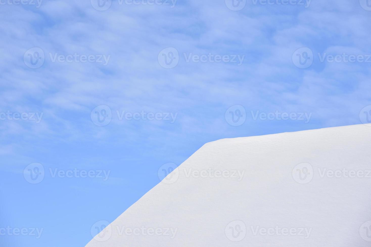 The roof of the house is in white snow with a blue sky. The roof of the house covered with snow in winter. A house with windows and snow on the roof. photo