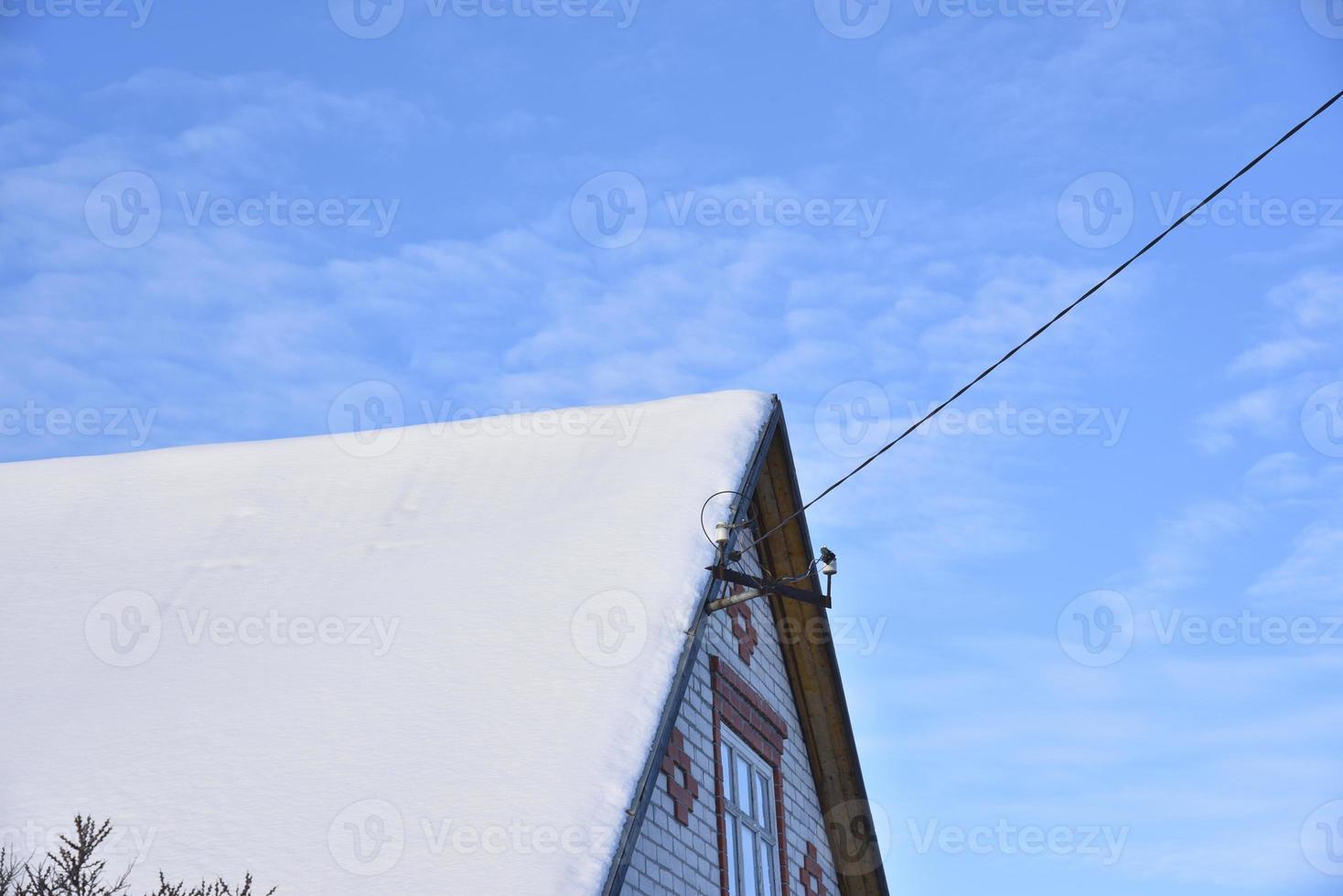 The roof of the house is in white snow with a blue sky. The roof of the house covered with snow in winter. A house with windows and snow on the roof. photo