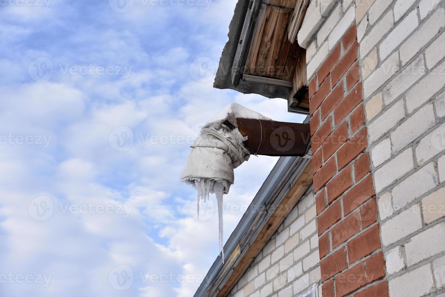 Spontaneous ventilation pipe in a house with icicles and ice in winter. The ventilation pipe is insulated in winter weather. photo