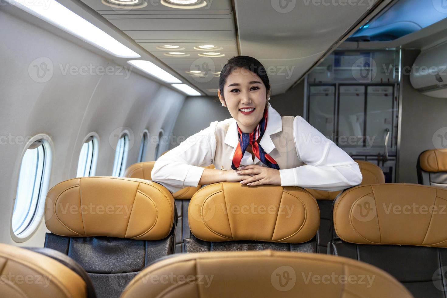 asistente de vuelo asiático posando con una sonrisa dentro del avión para dar la bienvenida al pasajero a bordo con asiento en el fondo para el concepto de viaje en avión foto