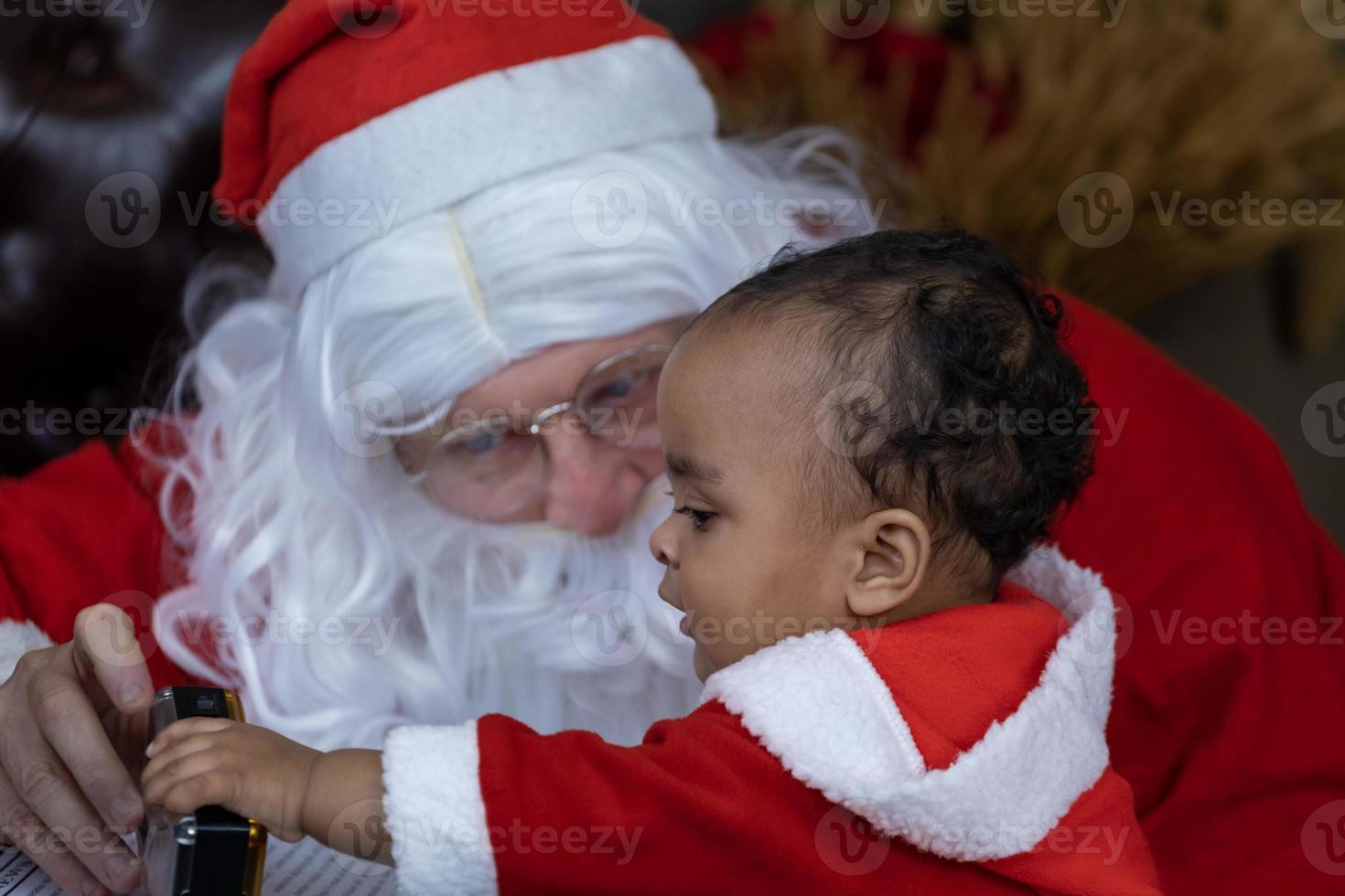 African American baby is opening the christmas present with Santa claus at night for season celebration photo