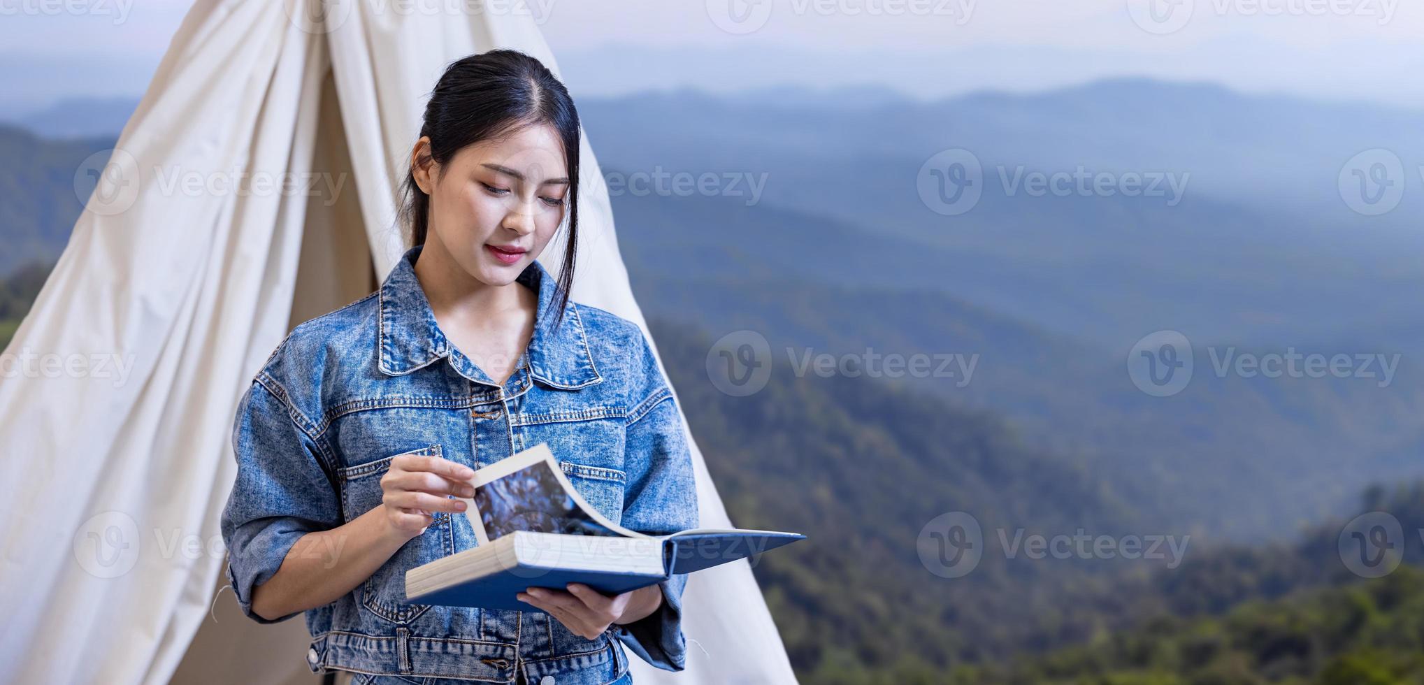 Asian woman reading book while on a solo trekking camp on the top of the mountain with small tent for weekend activities and outdoor pursuit photo