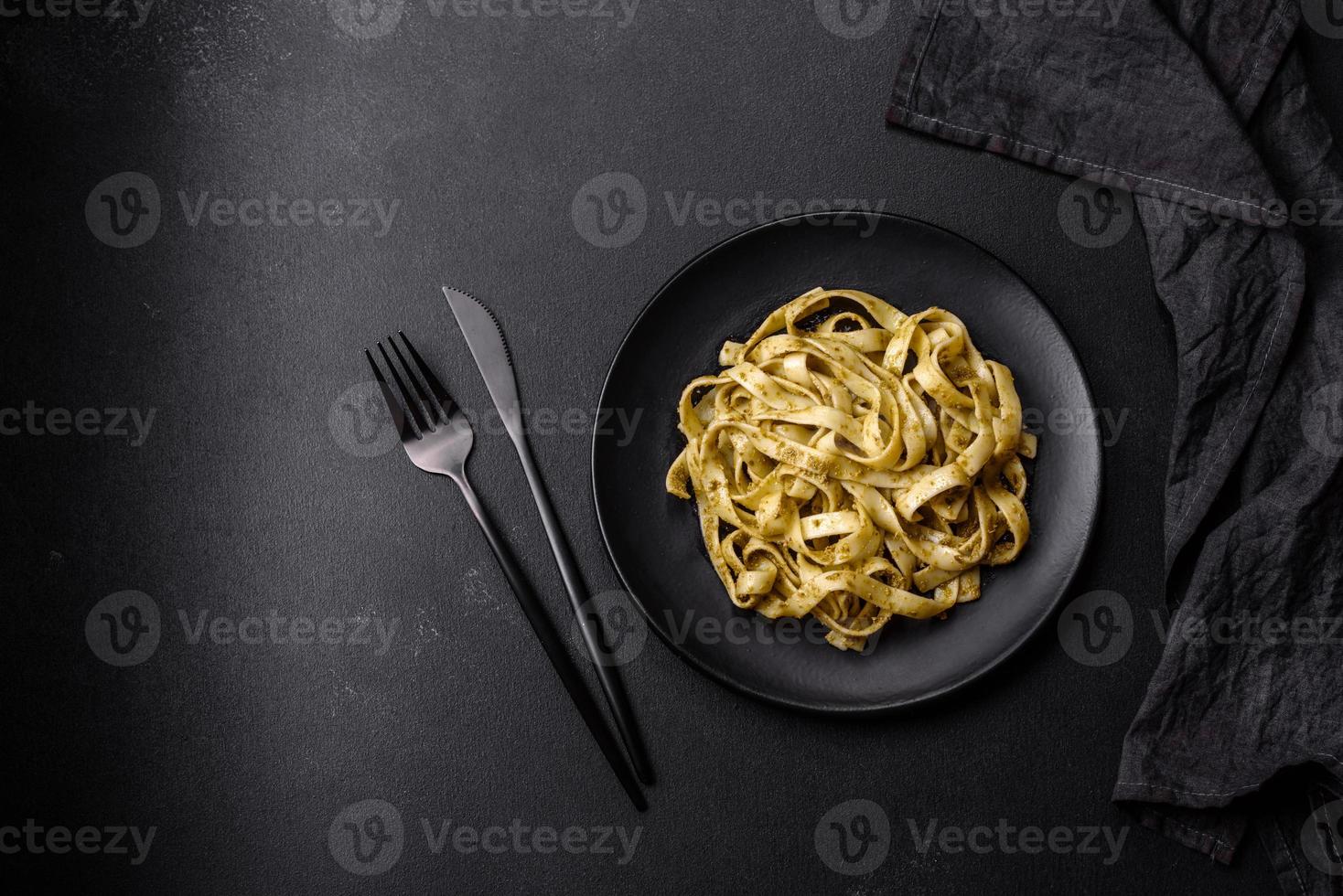 Delicious fresh pasta with pesto sauce and seafood on a black plate photo